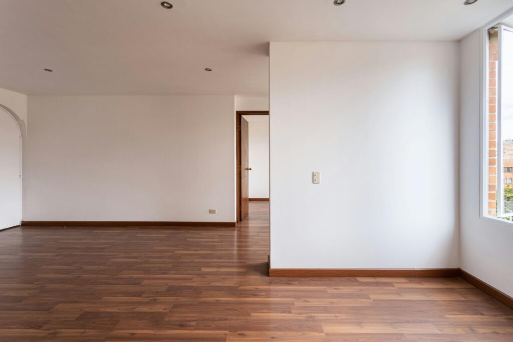Interior de vivienda con suelo de madera y paredes lisas blancas tras una reforma integral de estilo minimalista.