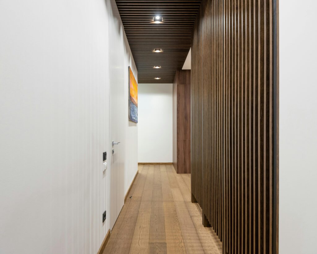 Pasillo moderno con suelo de parquet de madera y paredes con listones decorativos, ideal para proyectos de interiorismo en Vic