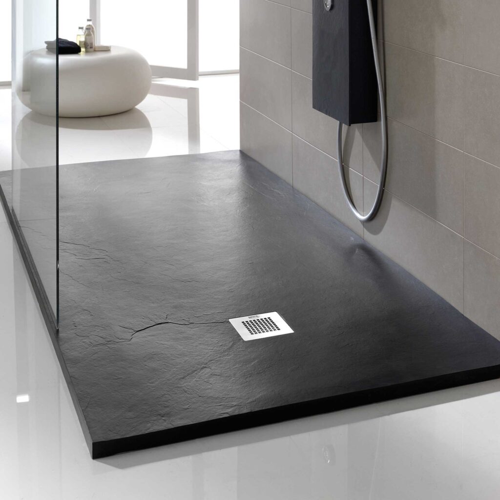 Plat de dutxa negre de textura pissarra instal·lat en bany modern amb revestiment ceràmic i mampara de vidre, disponible a Euromat Ripoll.