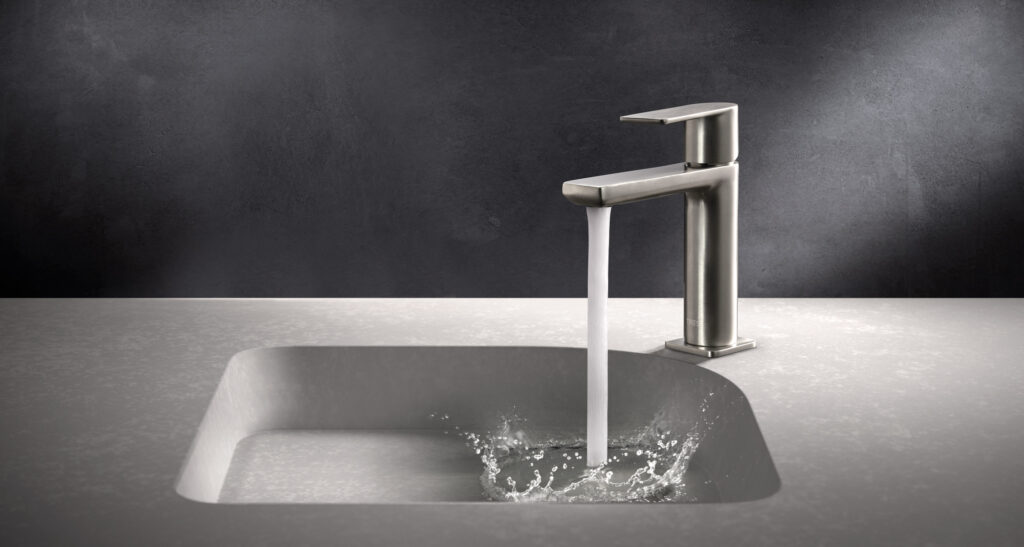 Aixeta lavabo moderna de metall amb aigua corrent sobre taulell gris.