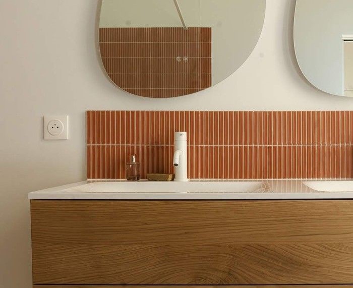 Lavabo de diseño moderno con mueble de madera y azulejos verticales color teja en baño reformado.